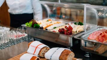 Un bufé con diversos alimentos, como pan, queso, uvas y jamón, junto con varias copas de agua.