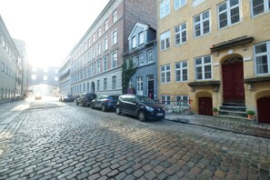 A cobblestone street lined with historic buildings, parked cars, and a bicycle.