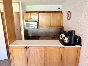 A compact kitchen with wooden cabinets, a microwave, a coffee maker, and a sink. - Pierrafort 31 - Charming 2-room apartment at the foot of the slopes (LES AVANCHERS VALMOREL)