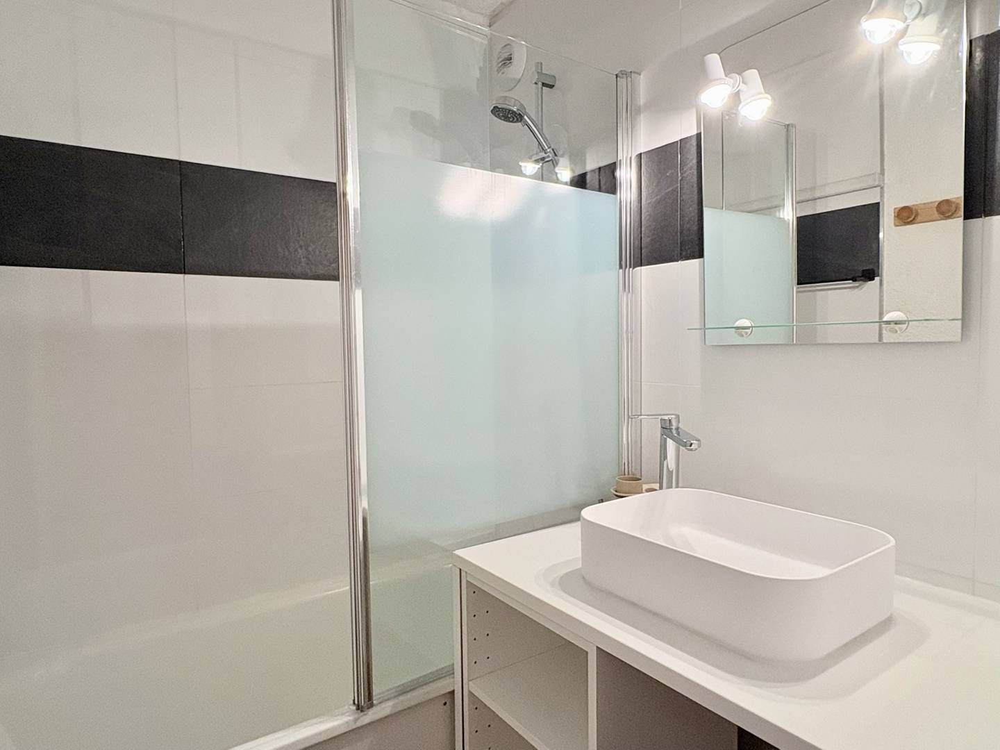 A modern bathroom with a glass shower enclosure, a white sink, and a mirror with a black and white stripe design.