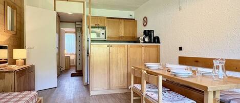 A compact room with a kitchenette, a dining table with chairs, and a bed with a plaid bedspread.