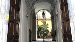 Un pasillo con detalles metálicos ornamentales, un candelabro y vista a un patio con plantas en macetas.