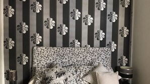 Un dormitorio con papel tapiz estampado, una cama con colcha, una mesita de noche con lámpara y una mesita auxiliar.