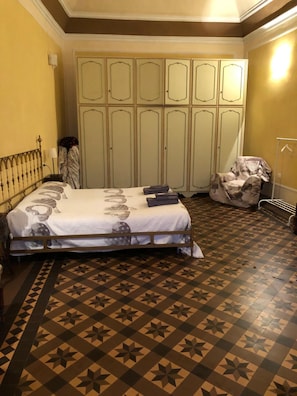 Une chambre avec un sol à motifs, un lit recouvert d’une courtepointe à fleurs, une armoire et une chaise.
