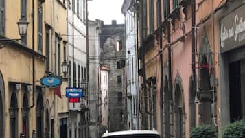 A narrow street with a parked car, buildings with traditional architecture, and a sign for 'Olivetti Associazione Pagani'.