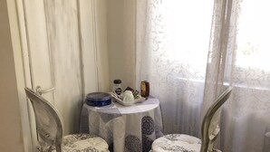 Un pequeño comedor con dos sillas y una mesa, una ventana con cortinas translúcidas y una puerta con marco blanco.