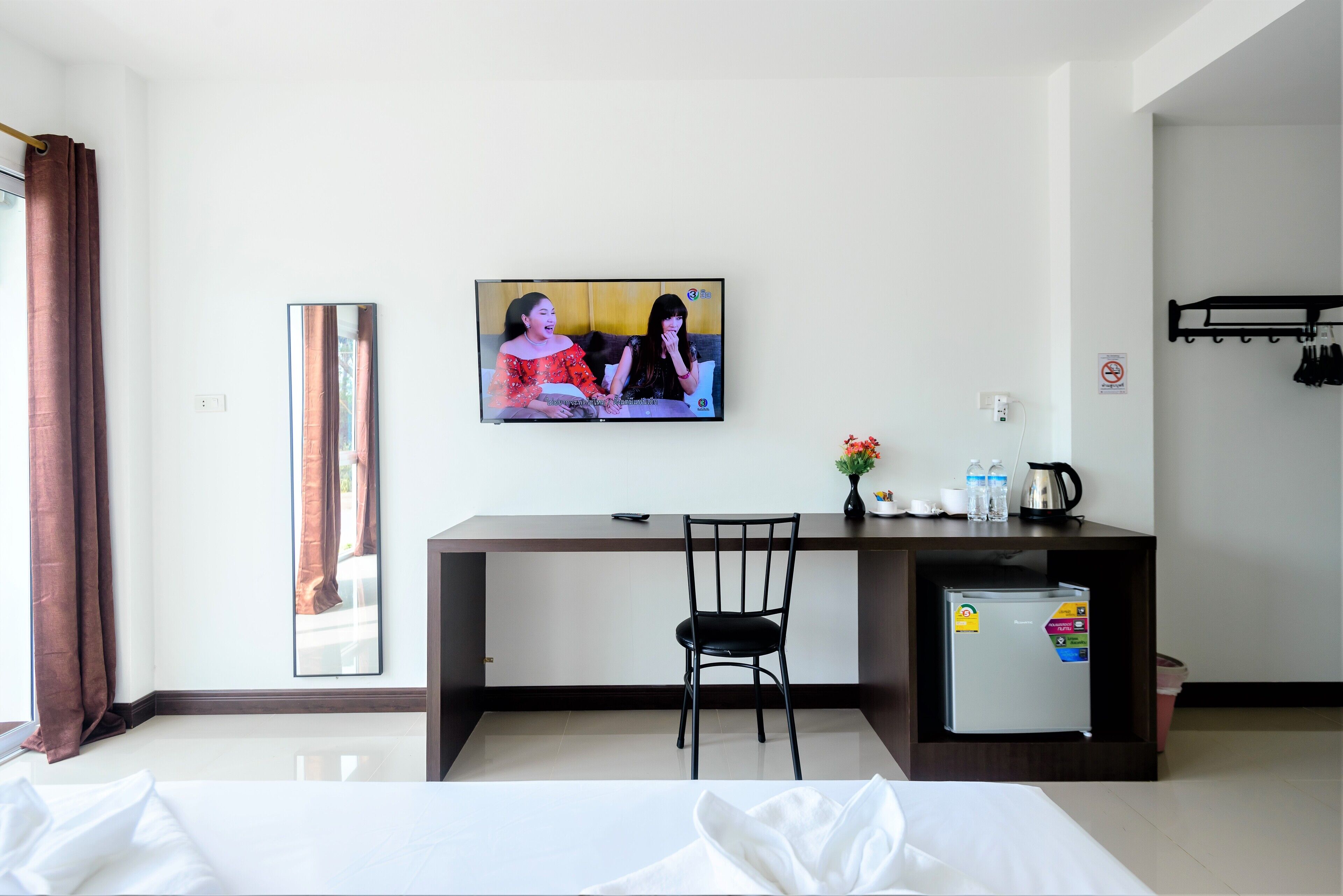 Habitación de hotel con cama, escritorio con silla, televisión, refrigerador y ventana con cortinas.