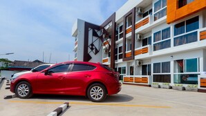 A red car parked in front of a modern building with multiple floors and large windows. - O2 Hotel Sakonnakhon (Sakon Nakhon)
