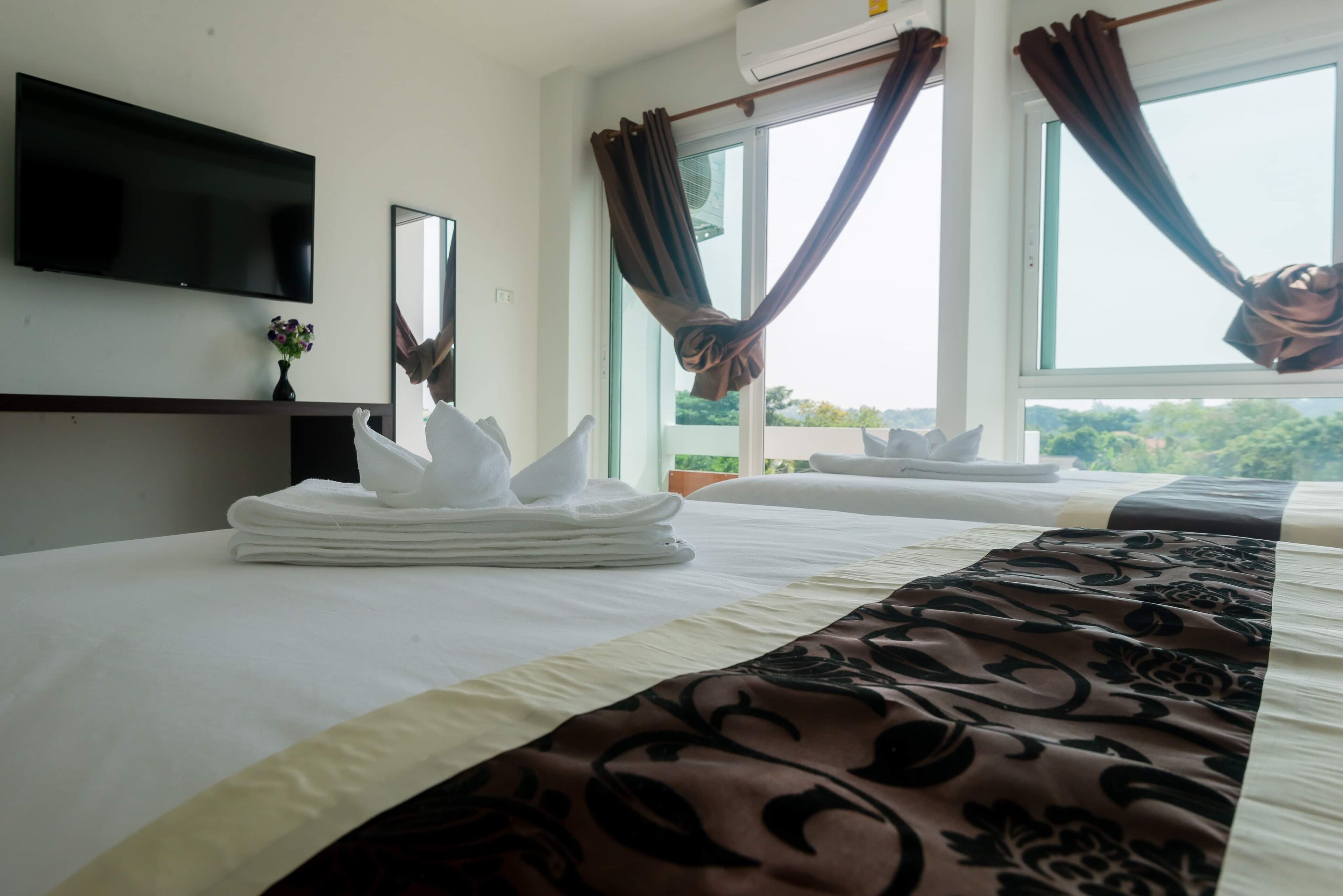 Habitación de hotel con cama, un televisor de pantalla plana en la pared, ventana con cortinas y vista a zonas verdes.