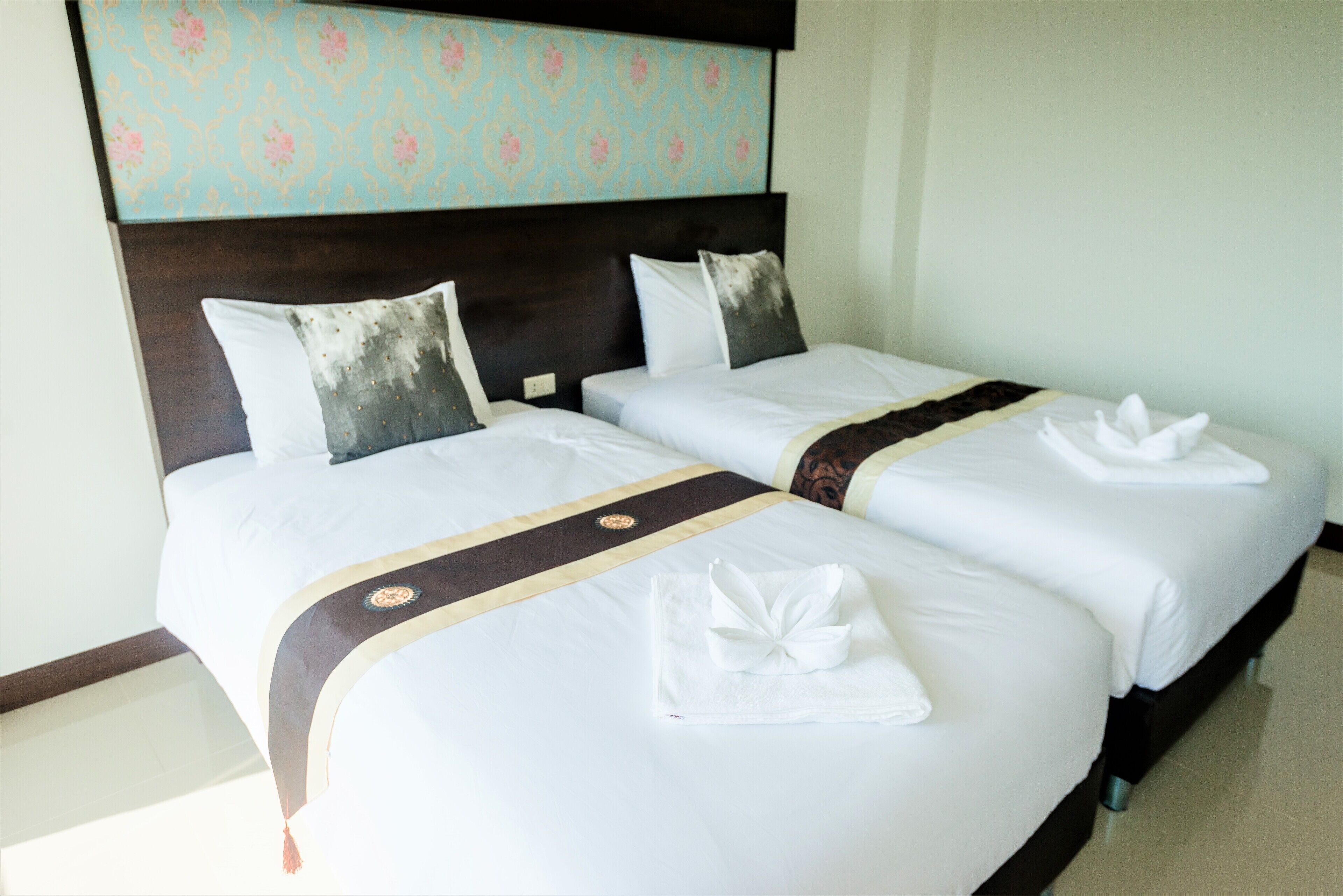 A hotel room with two beds, each with a white bedspread, pillows, and a brown decorative strip.