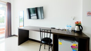 A modern room with a flat-screen TV mounted on the wall, a dark wooden desk, a black chair, and a small kitchenette area with a coffee maker and water bottles. - O2 Hotel Sakonnakhon (Sakon Nakhon)