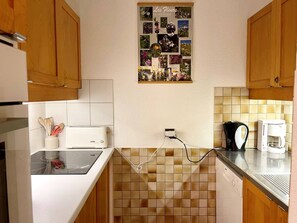 Een keuken met houten kastjes, een wit aanrecht, een broodrooster, een koffiezetapparaat en een wandcollage van bloemen.
