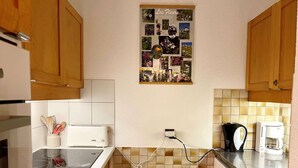 A kitchen with wooden cabinets, a white countertop, a toaster, a coffee maker, and a wall-mounted collage of flowers. - Les Côtes 15 - 2-room apartment with mountain view (LES AVANCHERS VALMOREL)