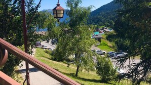 A scenic view from a balcony with a metal railing, overlooking a village with houses and parked cars, surrounded by greenery and mountains. - Les Côtes 15 - 2-room apartment with mountain view (LES AVANCHERS VALMOREL)