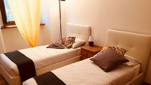 Deux lits jumeaux avec des têtes de lit, une table de chevet avec une lampe et une fenêtre avec des rideaux.