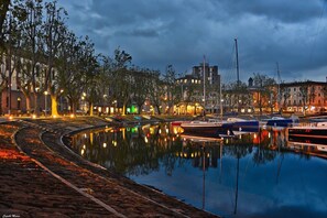 Ein Ufergebiet mit vertäuten Booten, einem Kanal und Gebäuden mit beleuchteten Fenstern.