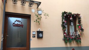 L’entrée d’un hôtel, avec une porte en bois, une pancarte indiquant « Joyeux Noël », un miroir fixé au mur décoré pour Noël et un banc à l’extérieur.