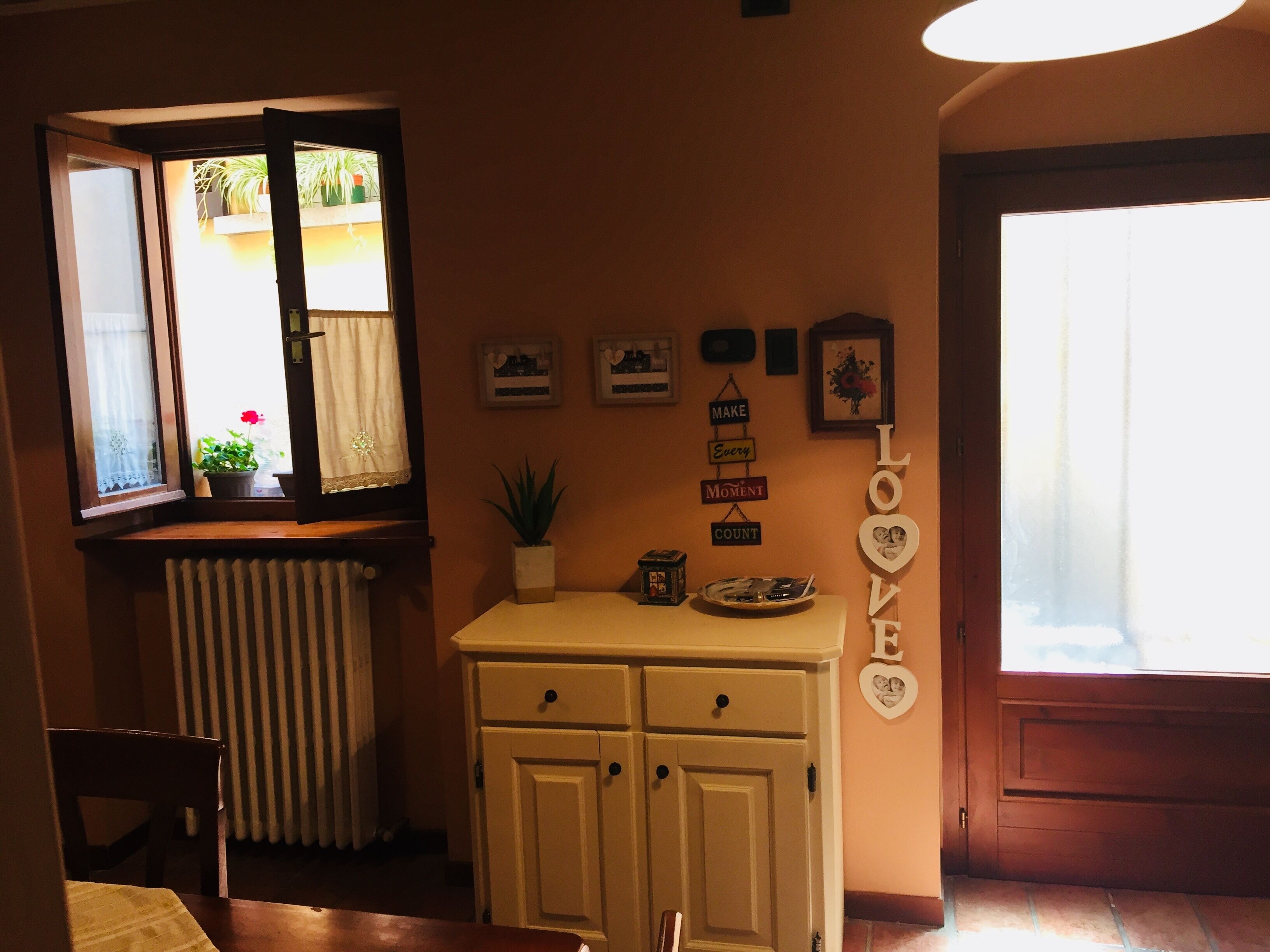 Una habitación acogedora con ventana, un radiador, una mesita con bandeja y una pared decorada con cuadros y un letrero que dice 'LOVE'.