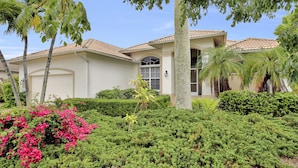 A two-story house with a tiled roof, surrounded by lush greenery and palm trees. - WIDE-VIEW ESTATE HOME NEAR BOAT RAMP WITH POOL & DEEP-WATER DOCKAGE (Marco Island)