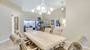 A dining area with a large wooden table and wicker chairs, a chandelier, and a view of the outdoors. - WIDE-VIEW ESTATE HOME NEAR BOAT RAMP WITH POOL & DEEP-WATER DOCKAGE (Marco Island)