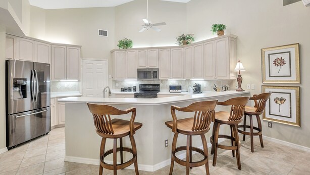 A modern kitchen with a central island, stainless steel appliances, and wooden bar stools. - WIDE-VIEW ESTATE HOME NEAR BOAT RAMP WITH POOL & DEEP-WATER DOCKAGE (Marco Island)