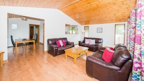 Ein geräumiges Wohnzimmer mit Holzboden, zwei Ledersofas mit Kissen, einem Holztisch und einem Essbereich mit Tisch und Stühlen.