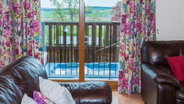 Ein Wohnzimmer mit einer Ledersofa, einem roten Kissen und Blick auf eine Whirlpool und eine Holzterrasse durch eine Glastür.