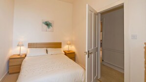 A bedroom with a bed, two bedside tables with lamps, a door leading to another room, and a wall-mounted light fixture. - Seabreeze (North Berwick)