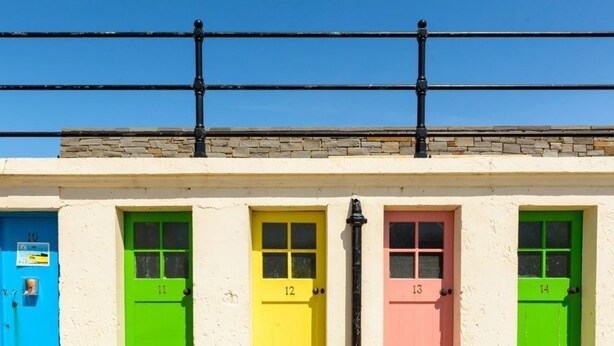 A row of brightly colored doors numbered 10 to 14, with a stone wall and a metal railing above. - Seabreeze (North Berwick)