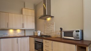 A modern kitchen with wooden cabinets, a gas stove, an oven, a microwave, and a tiled backsplash. - Seabreeze (North Berwick)