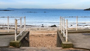 A concrete staircase leading to a sandy beach with a railing on both sides, overlooking a calm sea and distant land. - Seabreeze (North Berwick)