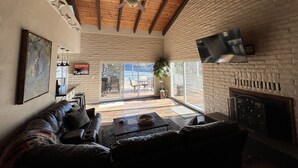 A spacious living room with a large window, a ceiling fan, a fireplace, and a television mounted on the wall.