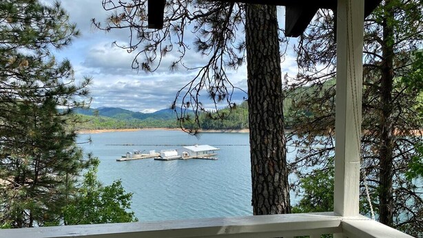 A wooden deck overlooking a lake with a dock and a houseboat.
