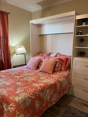 A bedroom with a bed, a nightstand, a lamp, a built-in wardrobe, and a shelf with plants.