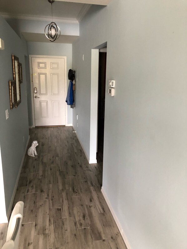 A hallway with a wooden floor, a white door, and a coat hanging on the wall.