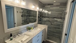Une salle de bain moderne avec un meuble-lavabo à deux vasques, un grand miroir et une douche à l’italienne.