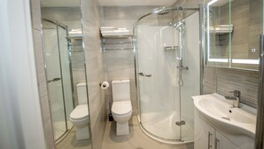 A modern bathroom with a glass-enclosed shower, a white toilet, and a sink with a mirror. - The James Suites (Londonderry)