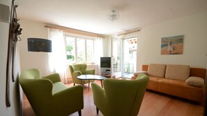 A living room with a sofa, two armchairs, a small table, a TV, and a painting on the wall.