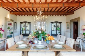 A dining room with a large wooden table set for a meal, flanked by two dark wooden cabinets with glass doors, a chandelier, and a white upholstered chair. - RENAISSANCE WINERY VILLA AMONG THE VINEYARDS, 9 BEDROOMS, 7 BATHS, WIFI, AIR CON (Lucca)