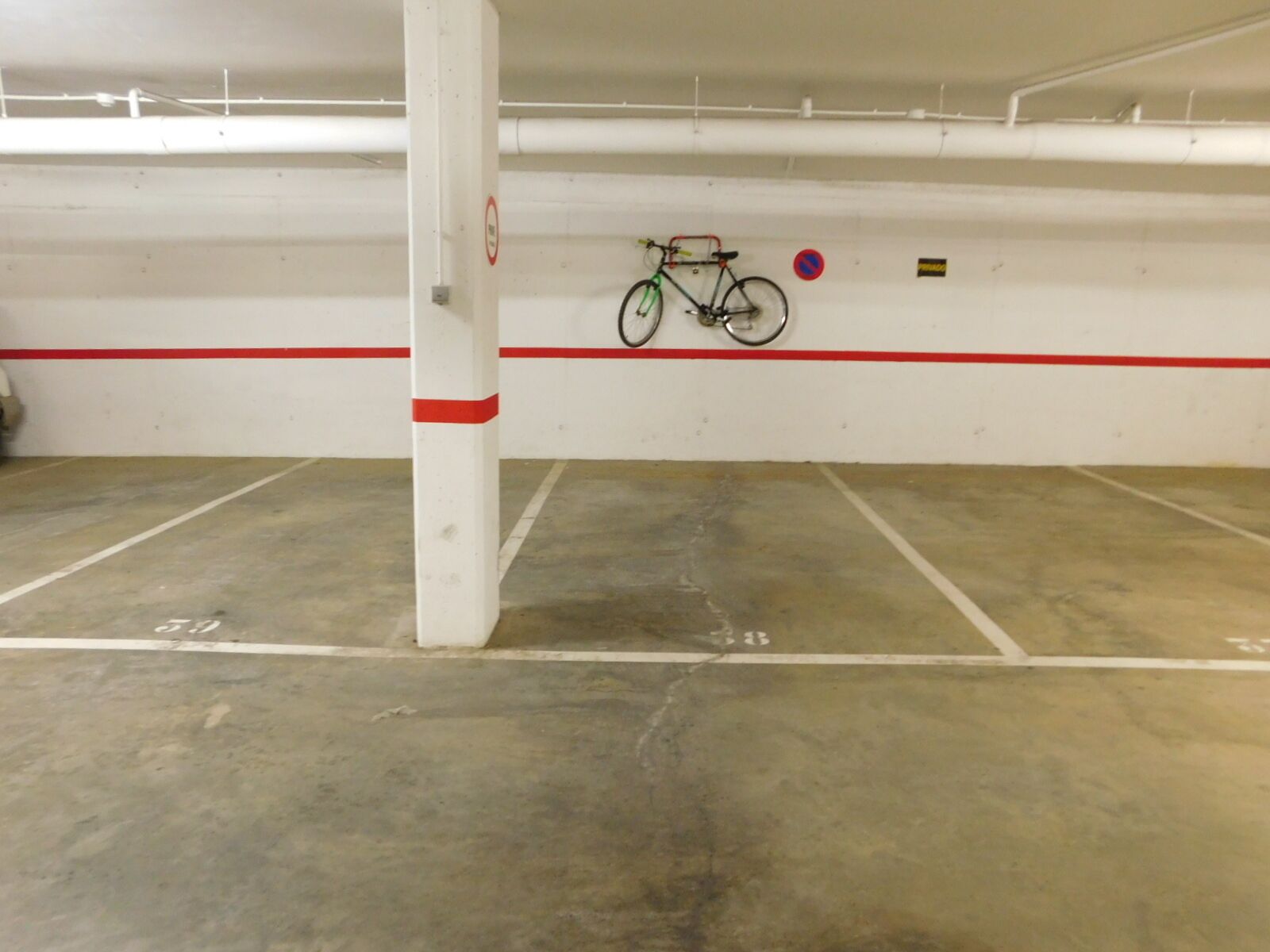 A parking garage with concrete floors, marked parking spaces, and a bicycle hanging on the wall.