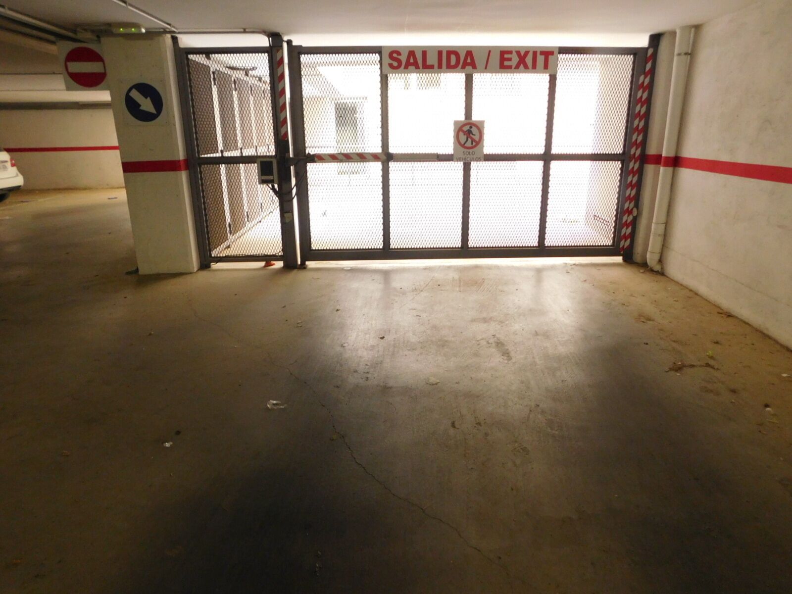 A parking garage exit with a 'SALIDA / EXIT' sign, a no entry sign, and a 'SOLO VEHICULOS' sign.