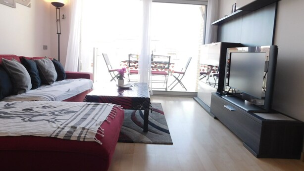 A living room with a red sofa, a flat-screen TV, and a dining area with a table and chairs. - A207 Apartment in the center of Roses with private parking, near the beach of Roses (Roses, Girona)
