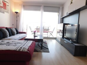 Uma sala de estar com um sofá vermelho, uma televisão de tela plana e um espaço de refeições com mesa e cadeiras.