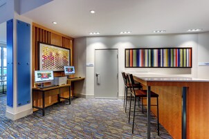 Un espacio de oficina moderno con dos puestos de trabajo por computadora, una mesa de reuniones y una llamativa obra de arte abstracta en la pared.