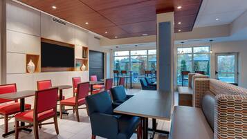 A modern dining area with tables and chairs, a large screen, and a view of the outdoors through large windows.