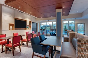 A modern dining area with tables and chairs, a large screen, and a view of the outdoors through large windows.