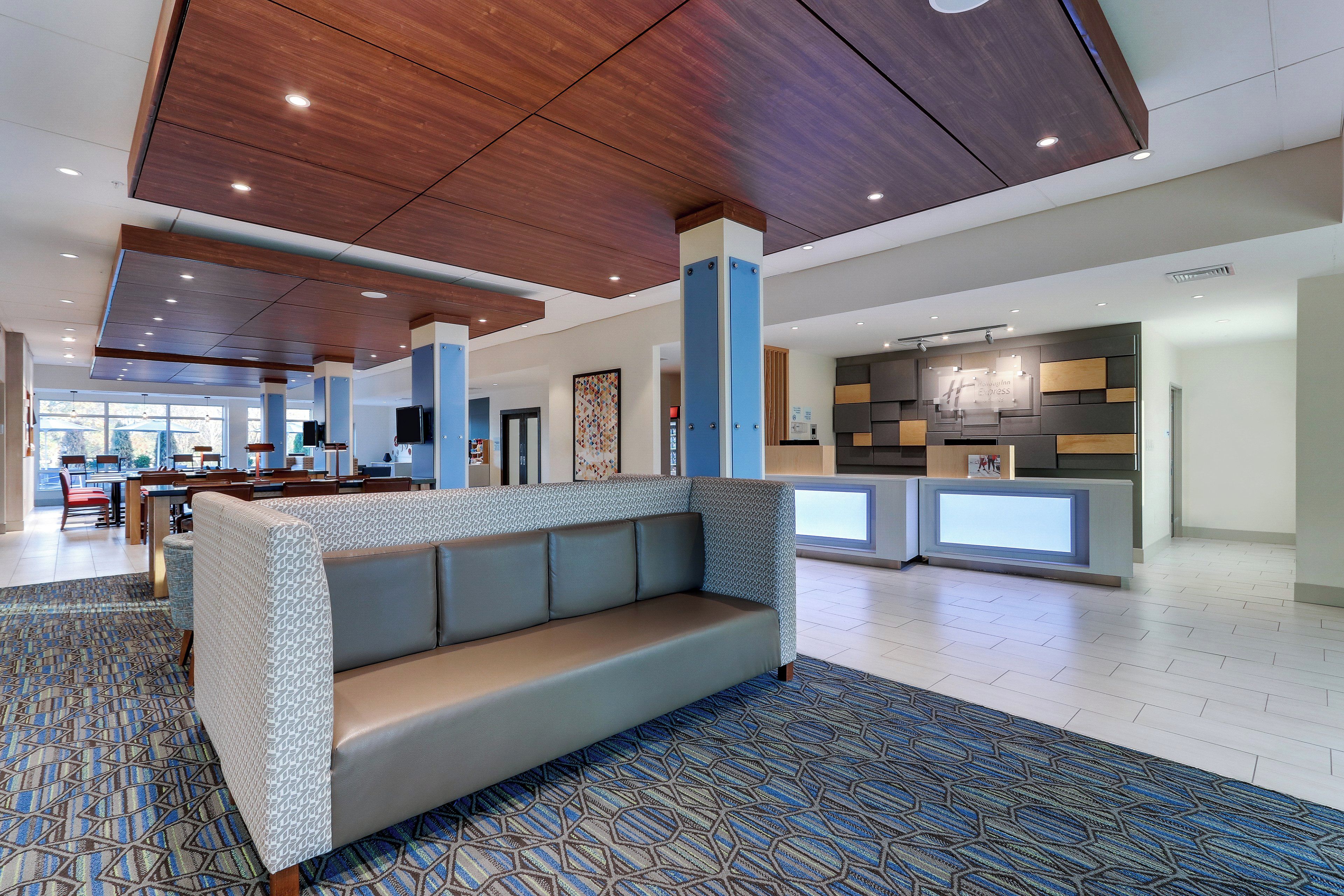 A modern lobby with a central seating area, a reception desk, and a dining area in the background.
