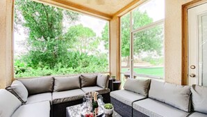 A sunroom with a large window, a sofa, and a table with a bottle and glasses.