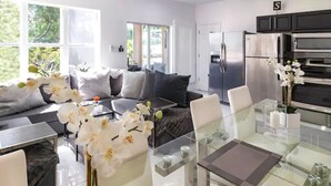 A modern kitchen with stainless steel appliances, a glass dining table, and a sofa with decorative pillows.
