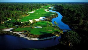 A golf course with a river, sand bunkers, and dense forest.